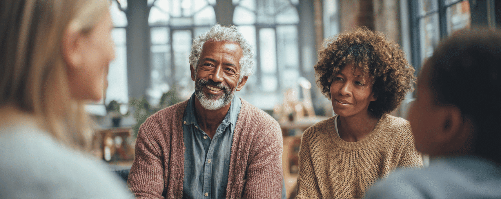 A smiling family of four sits together indoors, engaged in a warm, friendly conversation with a social worker.